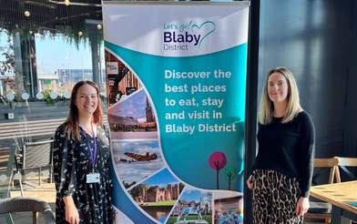 Two ladies standing next to a sign reading Discover the best places to eat, stay and visit in Blaby District